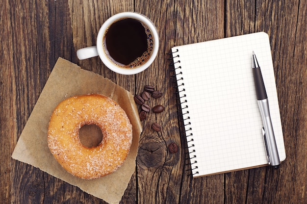 Geöffneter Notizblock mit Tasse Kaffee und Donut