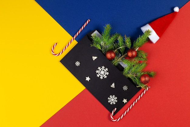 Geometrische kreative Weihnachtsflachlage mit schwarzem Umschlag. Oben Ansicht des mehrfarbigen geometrischen geschichteten Papierhintergrundes in Gelb, Blau, Rot. Weihnachten Neujahr minimales Konzept mit Kopienraum.