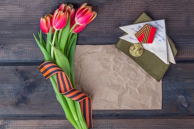 George Band, Briefpapier, rote Blumen Frontline-Buchstaben, Militärmütze und Befehle auf dem hölzernen Hintergrund. Victory Day oder Fatherland Defender Day Konzept.