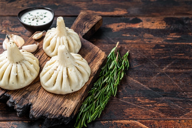 Georgian Khinkali Knödel mit Rind- und Lammfleisch auf Holzbrett mit Kräutern. Dunkler Holztisch. Draufsicht.