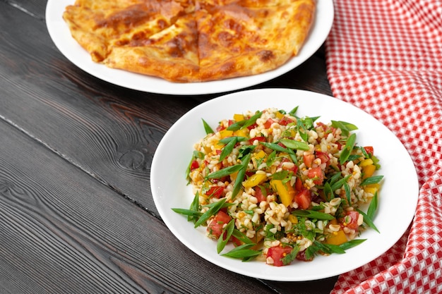 Georgian Tabouleh Salat mit Bulgur und Gemüse auf schwarzem Holztisch nah oben