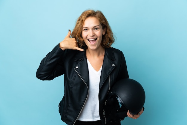 Georgianisches Mädchen, das einen Motorradhelm lokalisiert auf blauem Hintergrund hält, der Telefongeste macht. Rufen Sie mich zurück Zeichen