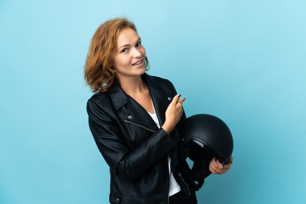 Georgianisches Mädchen, das einen Motorradhelm lokalisiert auf der blauen Wand hält, die zurück zeigt