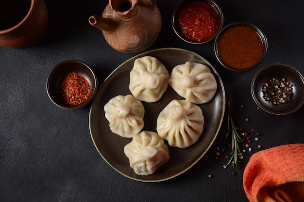 Georgische Teigtaschen Khinkali mit Fleisch und rotem Pfeffer, traditionelle georgische Küche. Khinkali mit lokalen Saucen - Tkemali, Satsebeli, Adzhika.