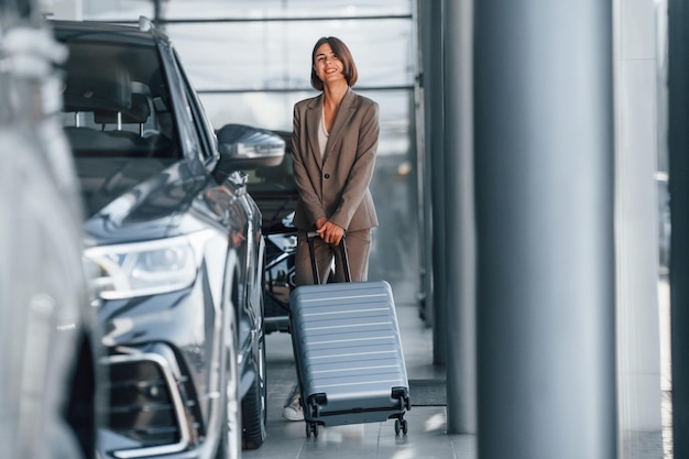 Gepäck halten Frau ist drinnen in der Nähe von brandneuen Automobilen drinnen