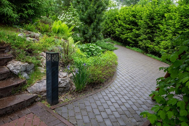 Gepflasterte, geschwungene Gasse und Stufen in einem Landschaftspark inmitten grüner Pflanzen Rastplatz, öffentlicher Park in der Stadt