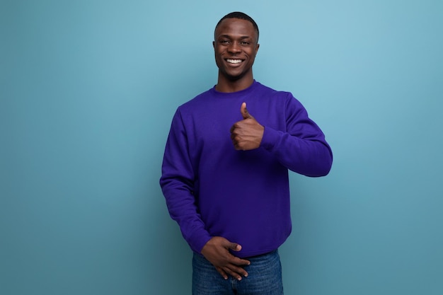 Gepflegter, freundlicher junger afrikanischer Mann in einem blauen Pullover auf blauem Hintergrund mit Kopierraum