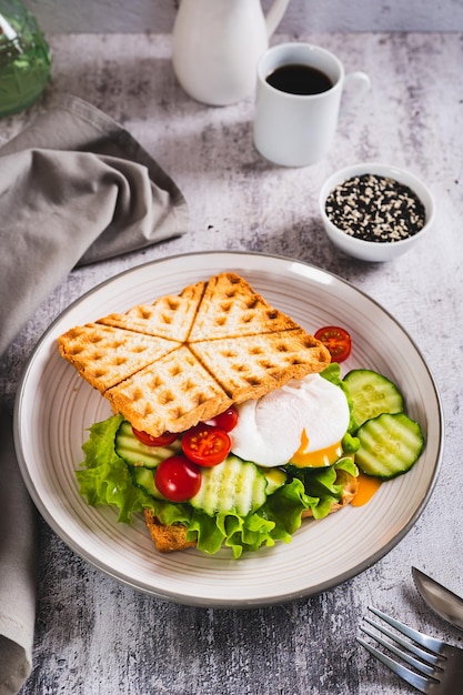 Foto gepochtes ei mit gurken, kirsch, tomaten und salat auf waffeltost auf einem platten in vertikaler ansicht