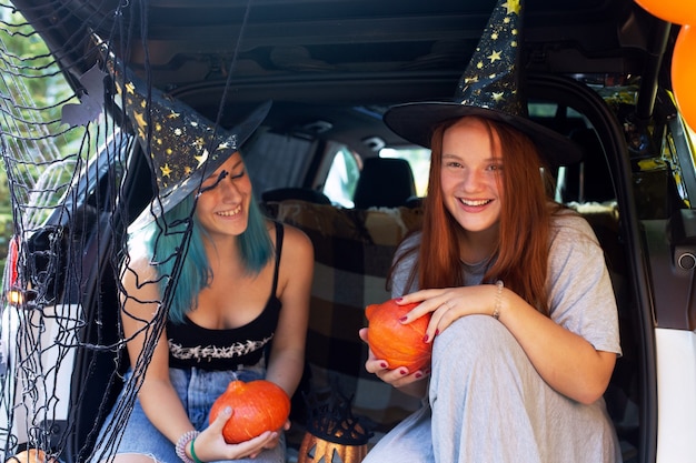 Geração Z de duas meninas comemorando o Halloween no porta-malas do carro. Decoração de férias de outono. Cabelo colorido. Foto de alta qualidade. Meninas olhando para a câmera sorrindo. Halloween seguro isolado. Doçura ou travessura