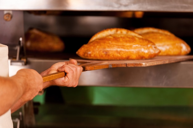 Gerade gebacken. Nahaufnahme des Mannes, der das frisch gebackene Brot aus dem Ofen nimmt