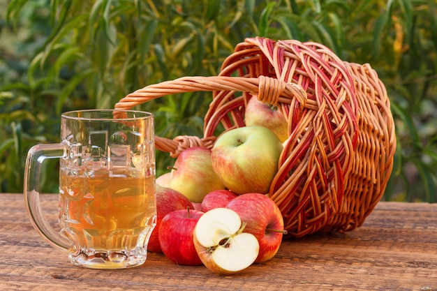 Gerade Äpfel in einem Weidenkorb gepflückt und Apfelwein im Glaskelch auf Holzbrettern