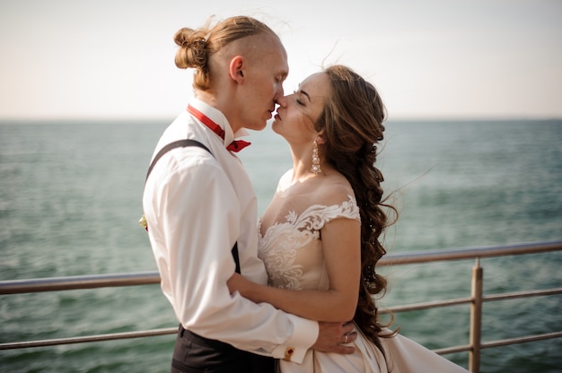 Foto gerade verheirateter glücklicher junge und mädchen, die sich auf dem pier am see küssen. vorstellung der hochzeit