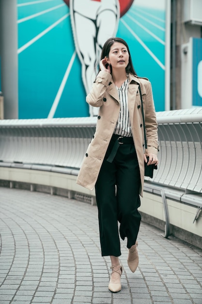 gerades Foto in voller Länge asiatische Koreanerin, die auf der Brücke in der modernen Stadt Osaka geht. Nippon Runner-Plakatwand im Hintergrund. schöne dame schnippt haare mit high heels schuhen auf der überführung im freien.