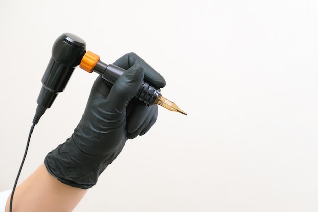 Gerät zum Tätowieren von Tätowierwerkzeugen auf weißem Hintergrund befindet sich in einer Hand in schwarzen Handschuhen