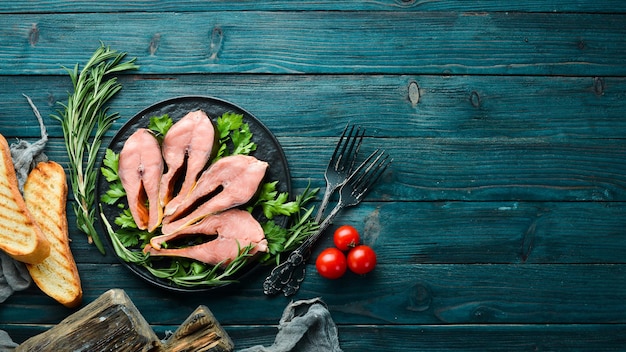 Geräucherte Fischsteaks auf einem schwarzen Teller. Roter Lachsfisch. Ansicht von oben. Freier Kopienraum.