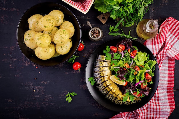 Geräucherte Makrele, gekochte Kartoffeln und frischer Salat auf dunklem Hintergrund