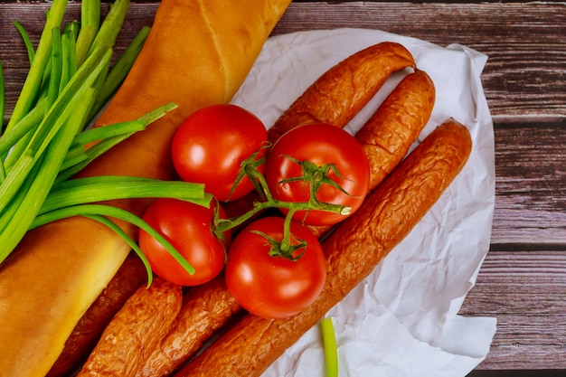 Geräucherte Wurst auf einem Holztisch mit Tomaten, Brot und Schnittlauch.