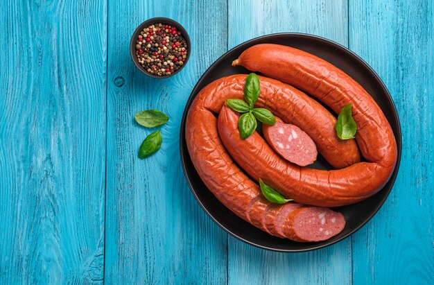 Geräucherte Wurst mit Basilikum und Gewürzen auf blauem Grund. Krakauer Wurst. Ansicht von oben, Kopienraum.