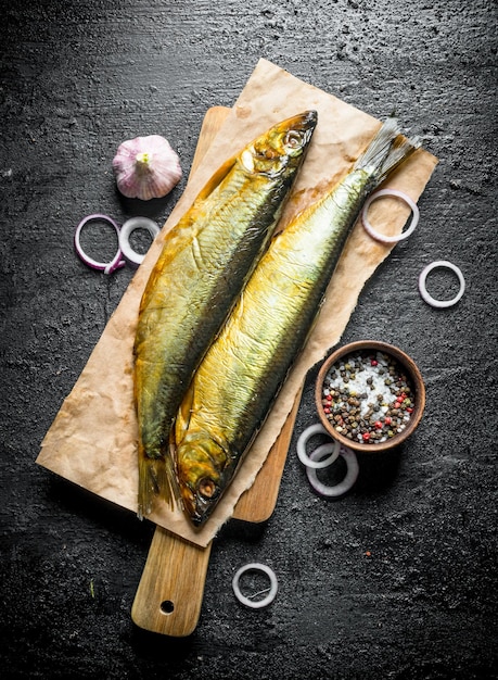 Geräucherter Fisch auf einem Schneidebrett mit Zwiebelringen, Gewürzen und Knoblauch