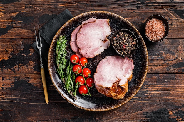 Geräuchertes Schweinefleisch - Schinken mit Kräutern auf rustikalem Teller. Hölzerner Hintergrund. Ansicht von oben.