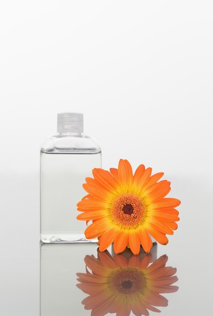 Foto gerbera naranja y un frasco de vidrio en un espejo