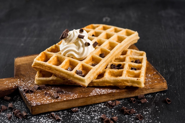 Gereizte hausgemachte Waffeln mit Sahne auf schwarzem Holzhintergrund