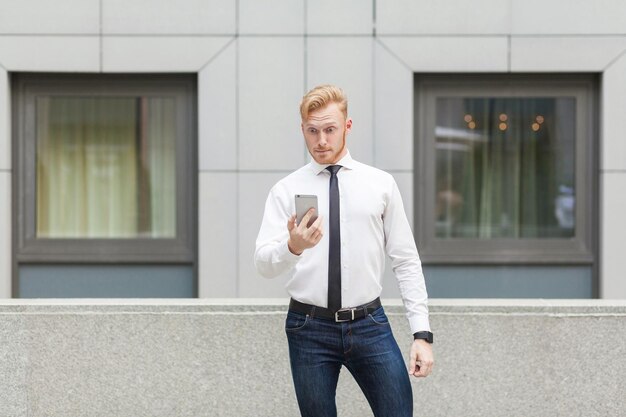 Gerente de adultos jóvenes cabeza roja mirando el teléfono inteligente con cara de sorpresa