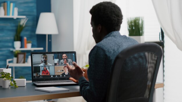 Gerente afroamericano en la conferencia de Internet en línea charlar con sus compañeros de trabajo trabajando a distancia desde h ...