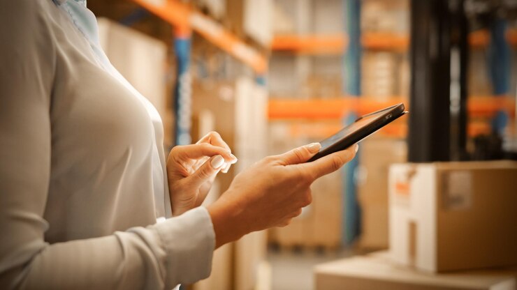 Foto el gerente de almacén utiliza una tableta digital con aplicación para comprobar el estado de entrega de paquetes con gráficos, infografías y estadísticas en la pantalla del centro de distribución con estantes con cajas de cartón