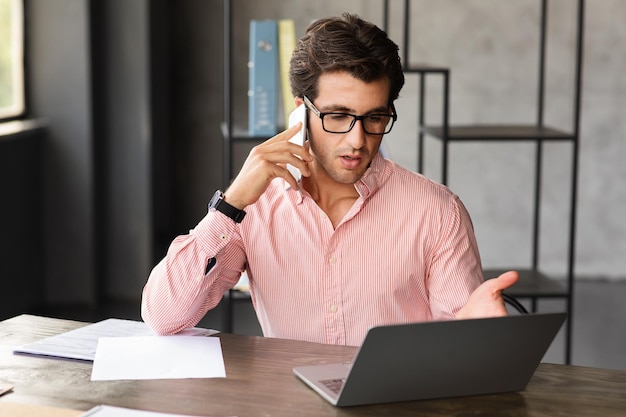 El gerente de CEO de un hombre guapo que trabaja desde la oficina tiene una llamada telefónica