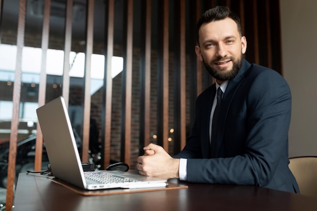 Gerente de una compañía de seguros en la oficina sentado en una computadora portátil mirando con una sonrisa