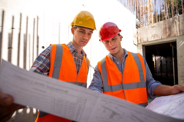 El gerente de construcción y el ingeniero vestidos con ropa de trabajo y cascos exploran la documentación del proyecto en el sitio de construcción. .