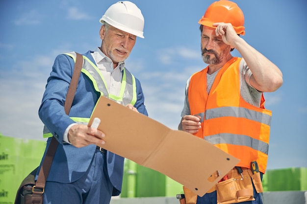 Gerente de construcción senior apuntando a algo a un trabajador masculino serio