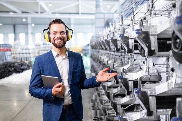 Foto gerente de fábrica caucasiano orgulhosamente de pé na linha de produção e mostrando nova máquina industrial