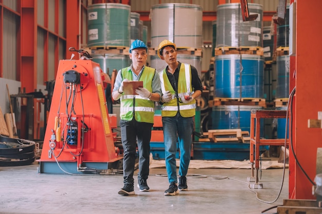 Gerente de fábrica de engenheiro asiático e funcionário de mecânico em capacete de segurança falando e inspeção dentro da fábrica