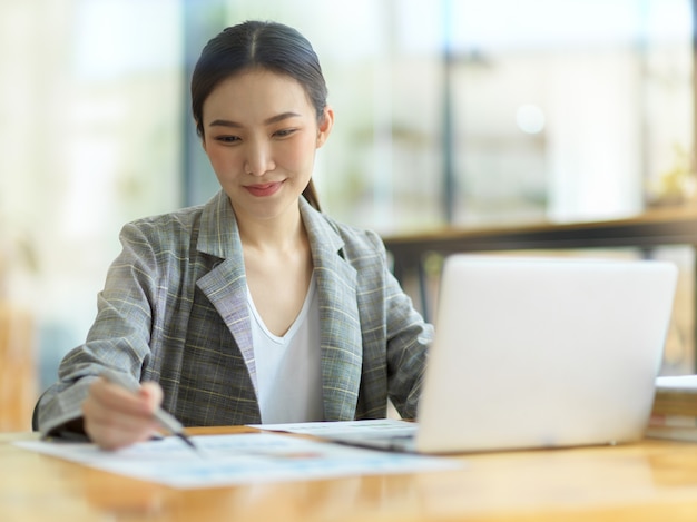 Gerente de finanças de jovens empresárias trabalhando em um laptop, olhando planilhas financeiras na mesa de trabalho no escritório