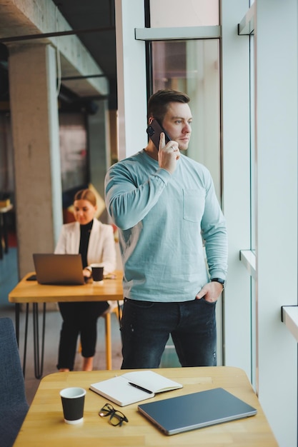 Gerente de homem de negócios olhando pela janela pensando profundamente em pé no local de trabalho com telefone no escritório pensando no futuro da empresa pensando em solução para tarefa de trabalho