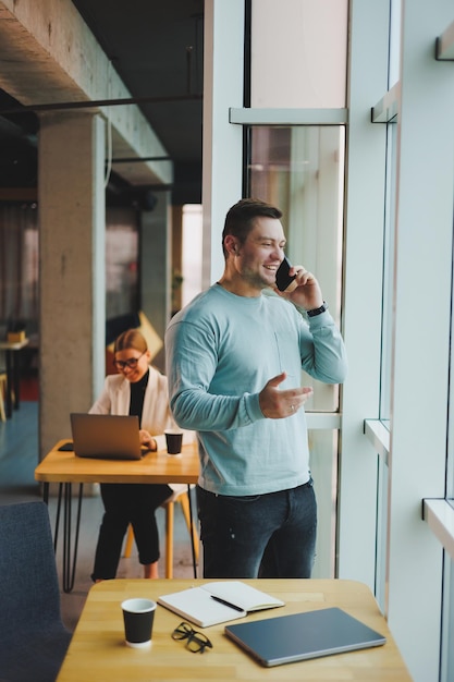 Gerente de homem de negócios olhando pela janela pensando profundamente em pé no local de trabalho com telefone no escritório pensando no futuro da empresa pensando em solução para tarefa de trabalho