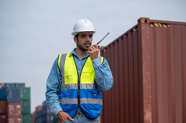 Gerente de logística falando no walkietalkie no armazém de contêineres para controlar o carregamento de contêineres no transporte do terminal do pátio de contêineres Recipiente do trabalhador falando rádio para gerenciar a exportação de mercadorias