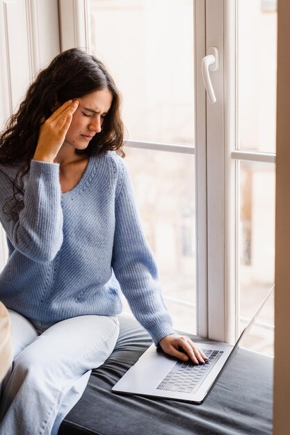 Gerente de mulher com forte dor de cabeça trabalhando no laptop on-line remotamente no café com janela grande Menina triste com laptop com enxaqueca toca a cabeça por causa da dor