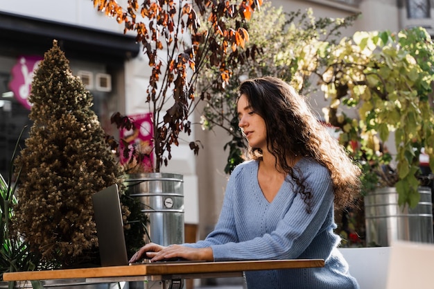 Gerente de mulher de negócios confiante com laptop está trabalhando com colegas on-line no café Garota atraente freelancer está trabalhando on-line no laptop no café ao ar livre