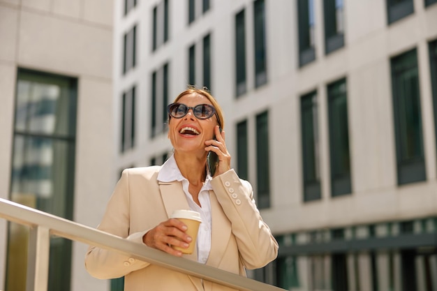 Foto gerente de mulher falando ao telefone enquanto está em um edifício moderno e bebendo café