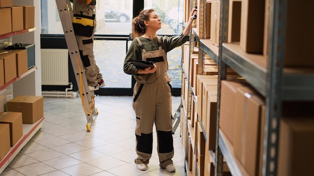 Gerente de mulher trabalhando no inventário de estoque com scanner de tablet, verificando códigos de barras de produtos em pacotes. Trabalhadora analisando caixas com mercadorias de carga no depósito de depósito.