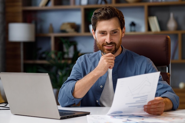 Foto gerente de negócios masculino bonito trabalhando atrás de um laptop em um elegante trabalho remoto de escritório em ho