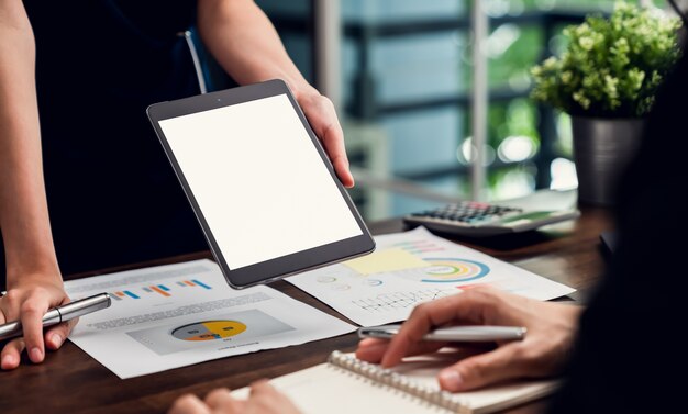 Gerente de negócios segurando a tela em branco do tablet e encontrando-se na mesa no escritório