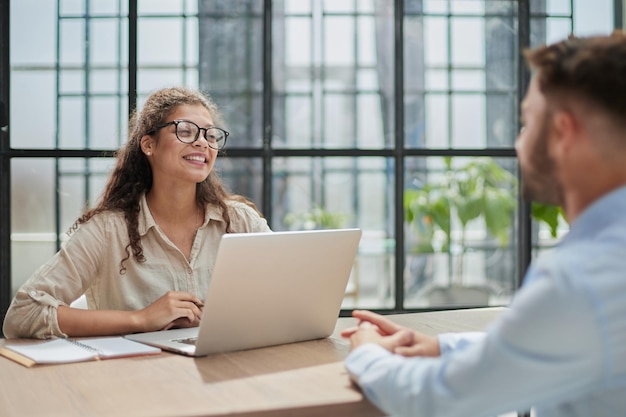 Gerente de óculos sentado à mesa recebe um cliente no escritório