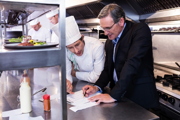 Gerente de restaurante masculino escrevendo na área de transferência enquanto interage com o chefe de cozinha