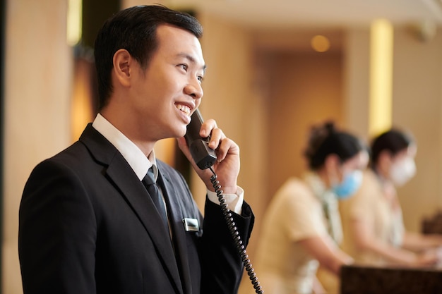 Gerente de um hotel de spa vietnamita a falar ao telefone com um hóspede a pedir o pequeno-almoço no quarto