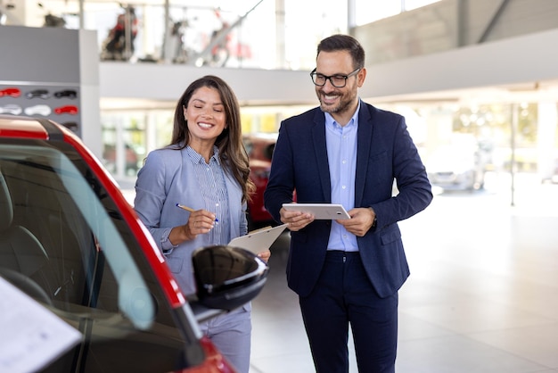 Gerente de vendas de carros mostrando carro a uma compradora caucasiana de pé em uma concessionária de automóveis de luxo comprando um conceito de veículo