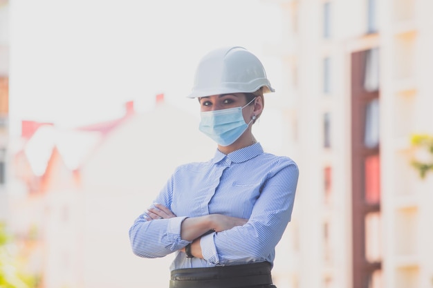 Gerente de vendas em pé perto do prédio enquanto obras de construção aguardam clientes Agente imobiliário mulher em roupas de estilo comercial usando capacete de proteção e máscara médica